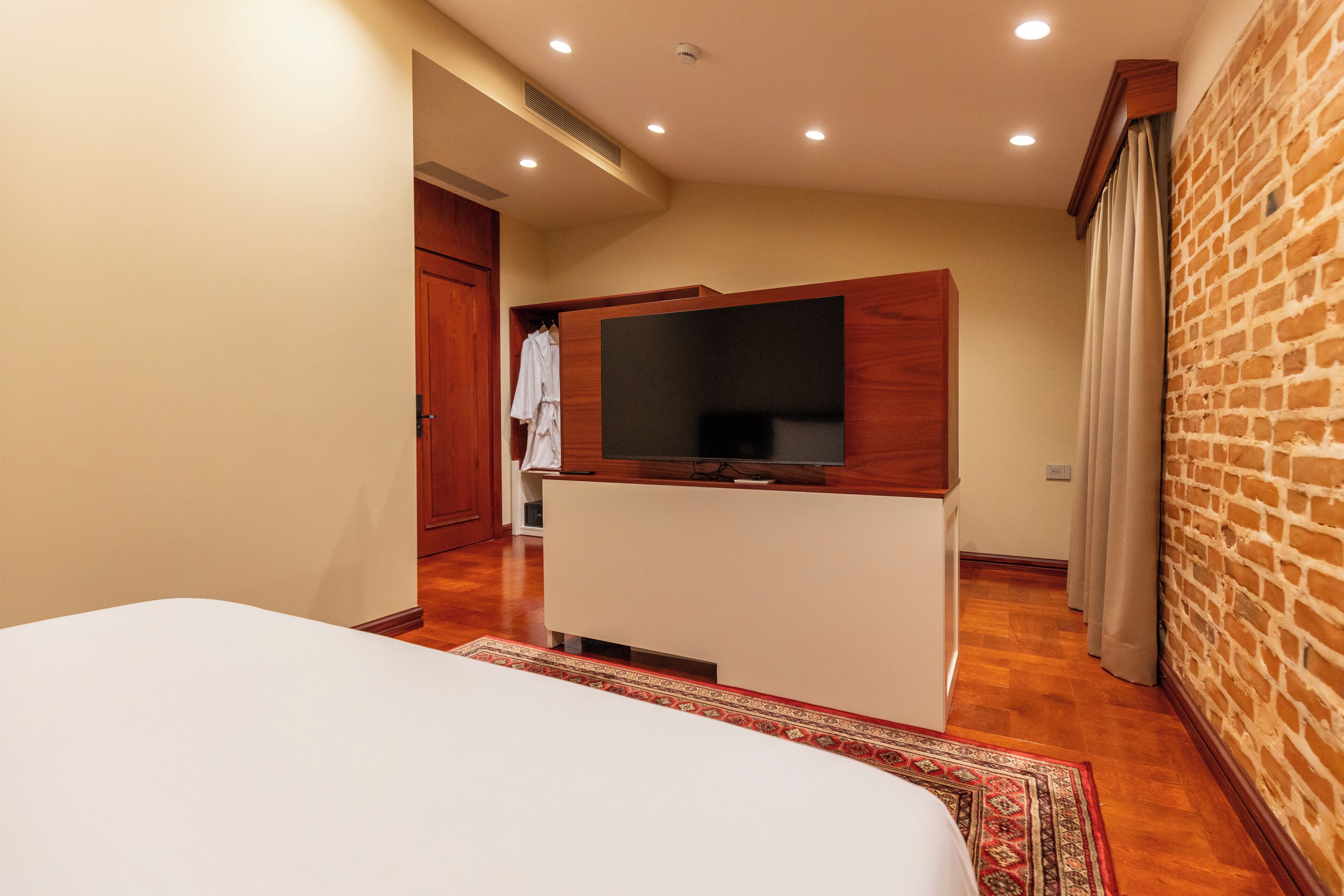 Habitación de hotel con una cama, un televisor sobre un mueble de madera, una pared de ladrillo y una puerta que da a un baño.