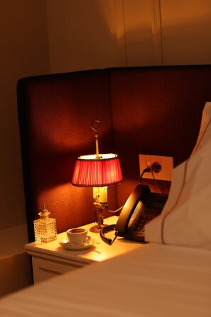 A hotel room with a bedside table, a lamp, a telephone, a cup of coffee, and a decorative bottle. - Vatër Hotel (Shkodër)
