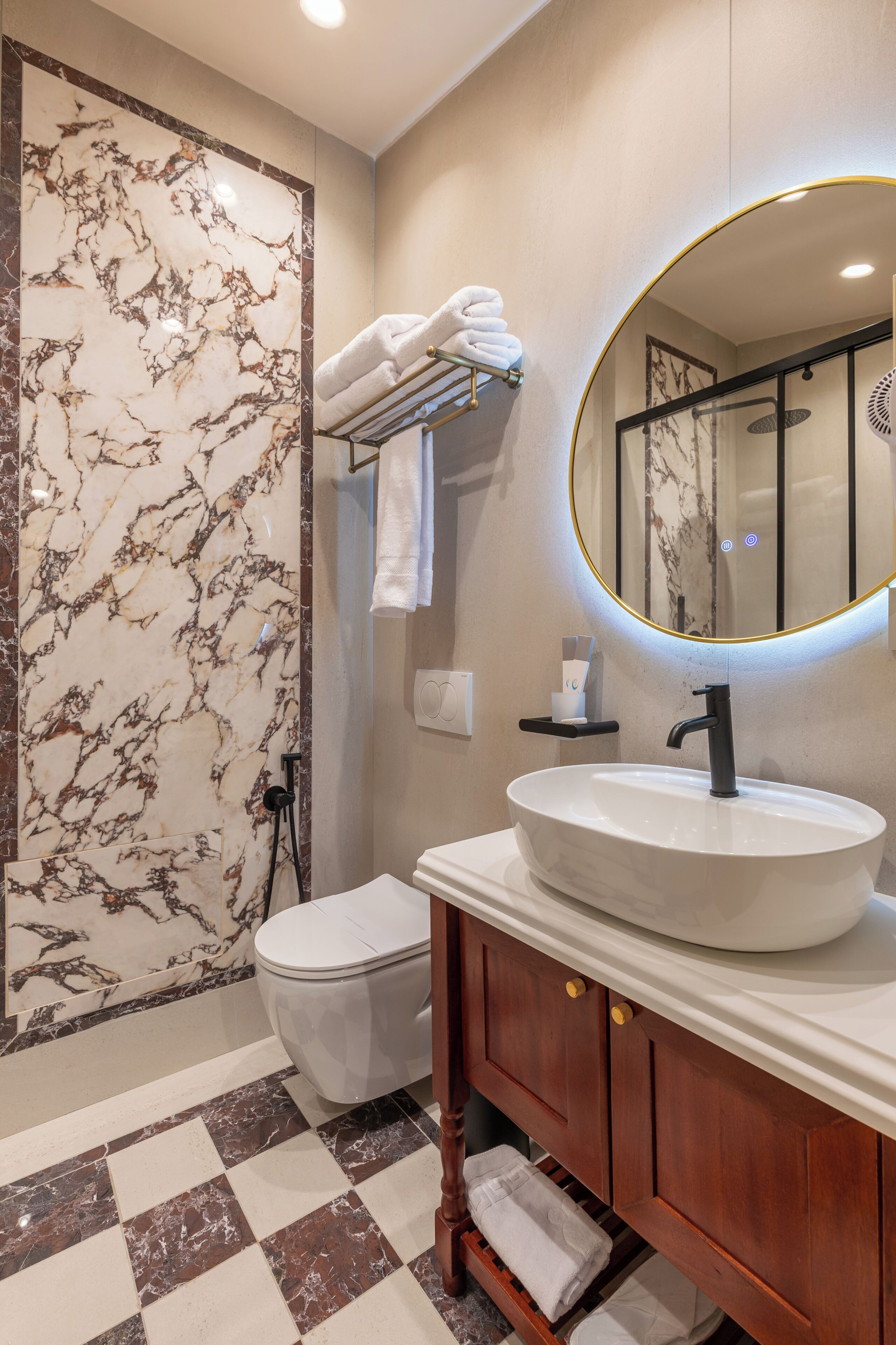 A bathroom with a marble wall, a white sink, a wooden vanity, and a toilet.