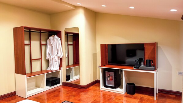 A hotel room with a wooden wardrobe, a television, a coffee maker, and a mirror. - Vatër Hotel (Shkodër)