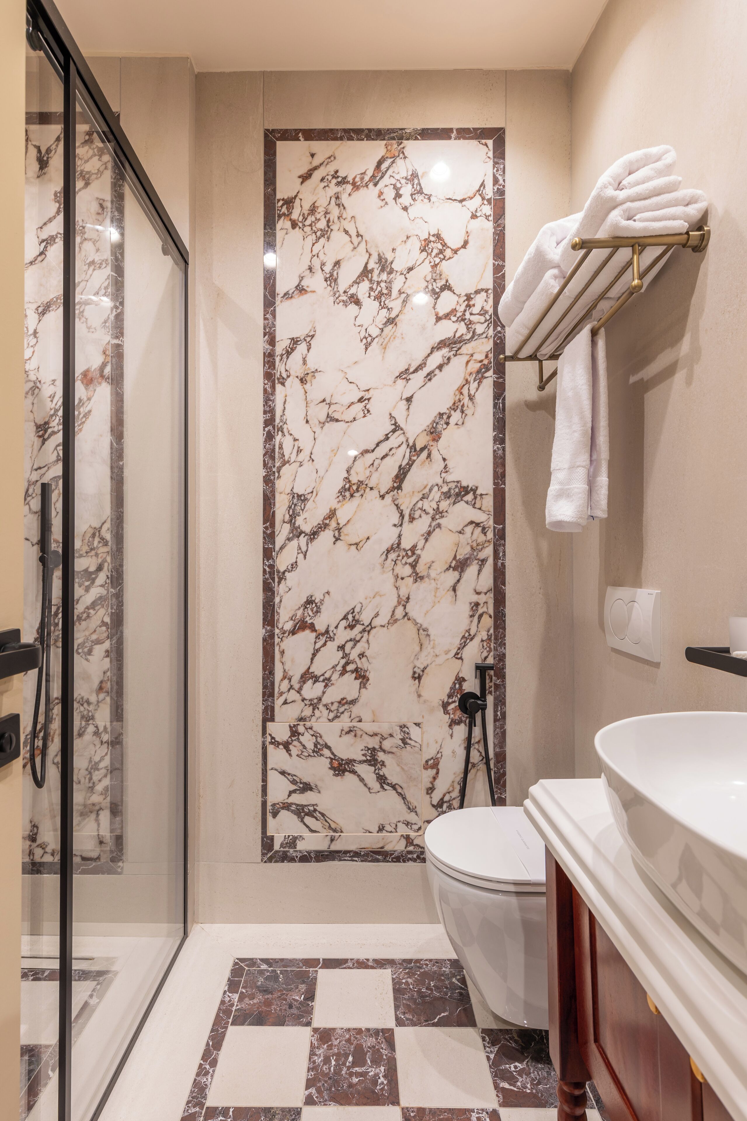 A bathroom with a glass shower enclosure, a toilet, a sink, and a towel rack.