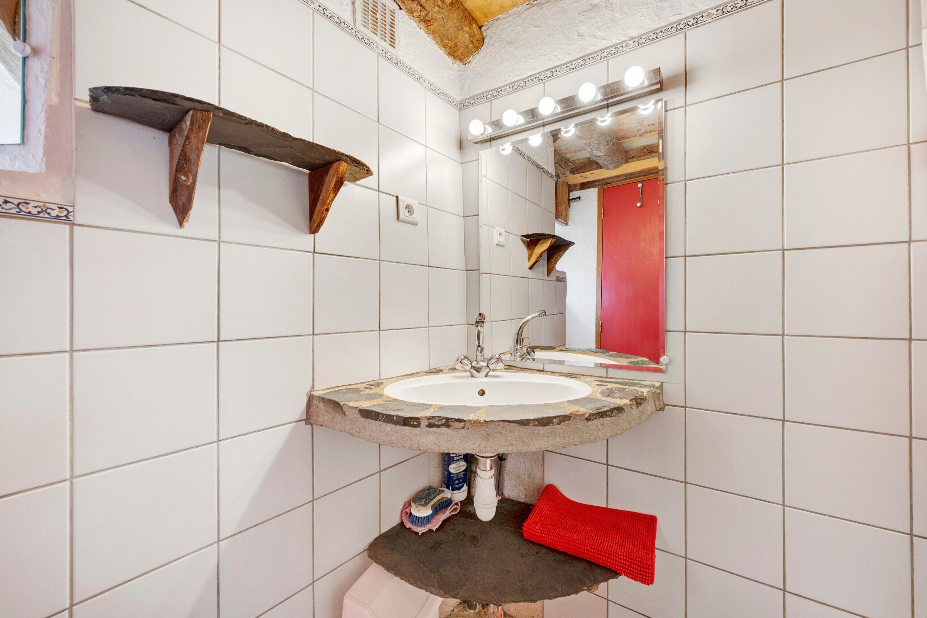 Ein Badezimmer mit einem Steinkonstruktion als Waschbecken, einem beleuchteten Spiegel und einem roten Handtuch.
