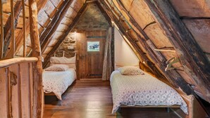 Ein rustikales Schlafzimmer im Dachgeschoss mit Holzbalken, zwei Betten und einer Holztür.