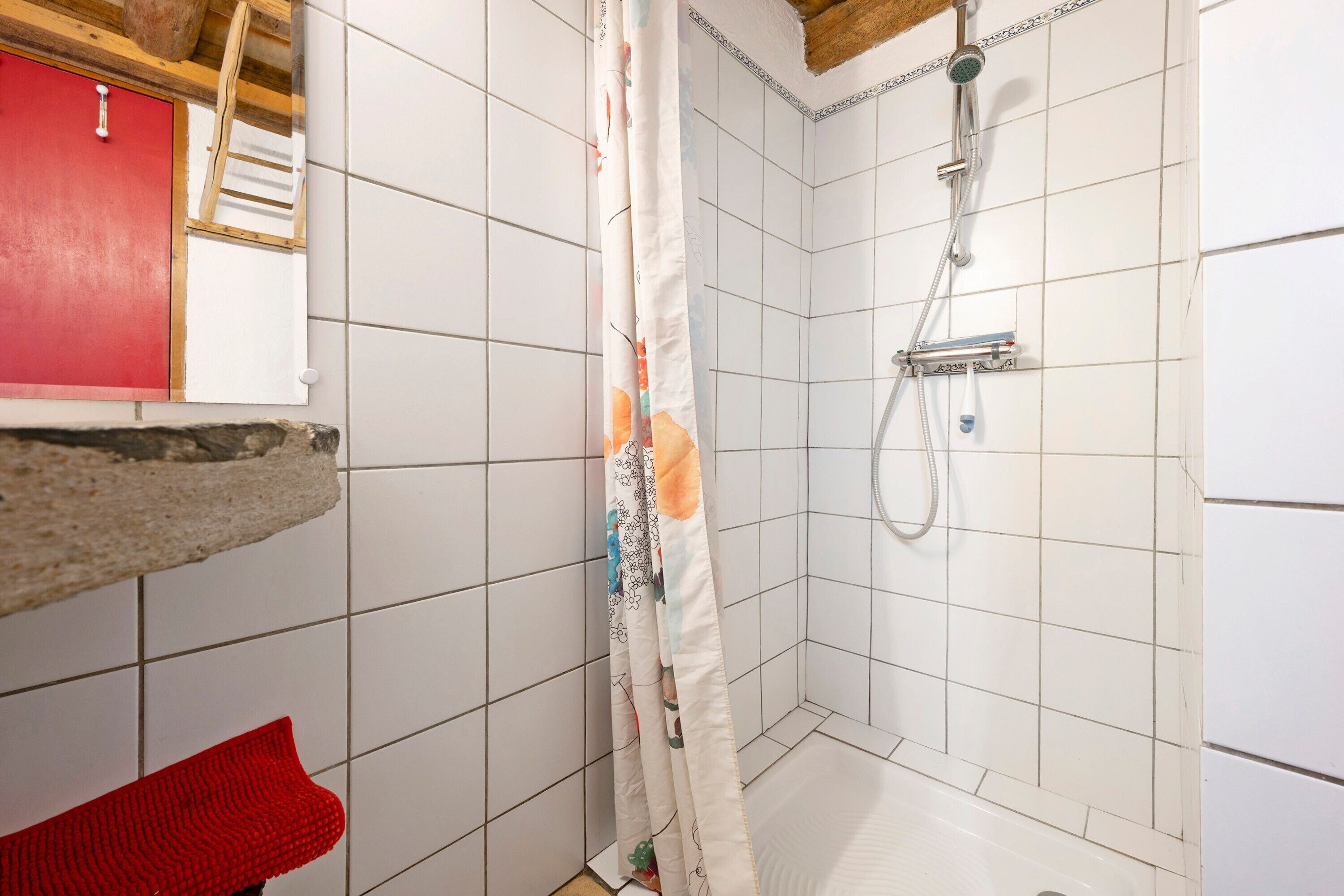 Une douche avec un rideau, des murs carrelés, un banc rouge et un plafond avec une poutre en bois.
