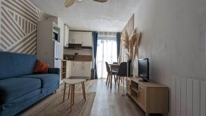 Een moderne woonkamer met een blauwe bank, een bijzettafeltje, een televisie en een plafondventilator.