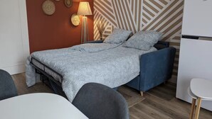 Een slaapkamer met een bed, bedlamp, wanddecoratie en een kitchenette.