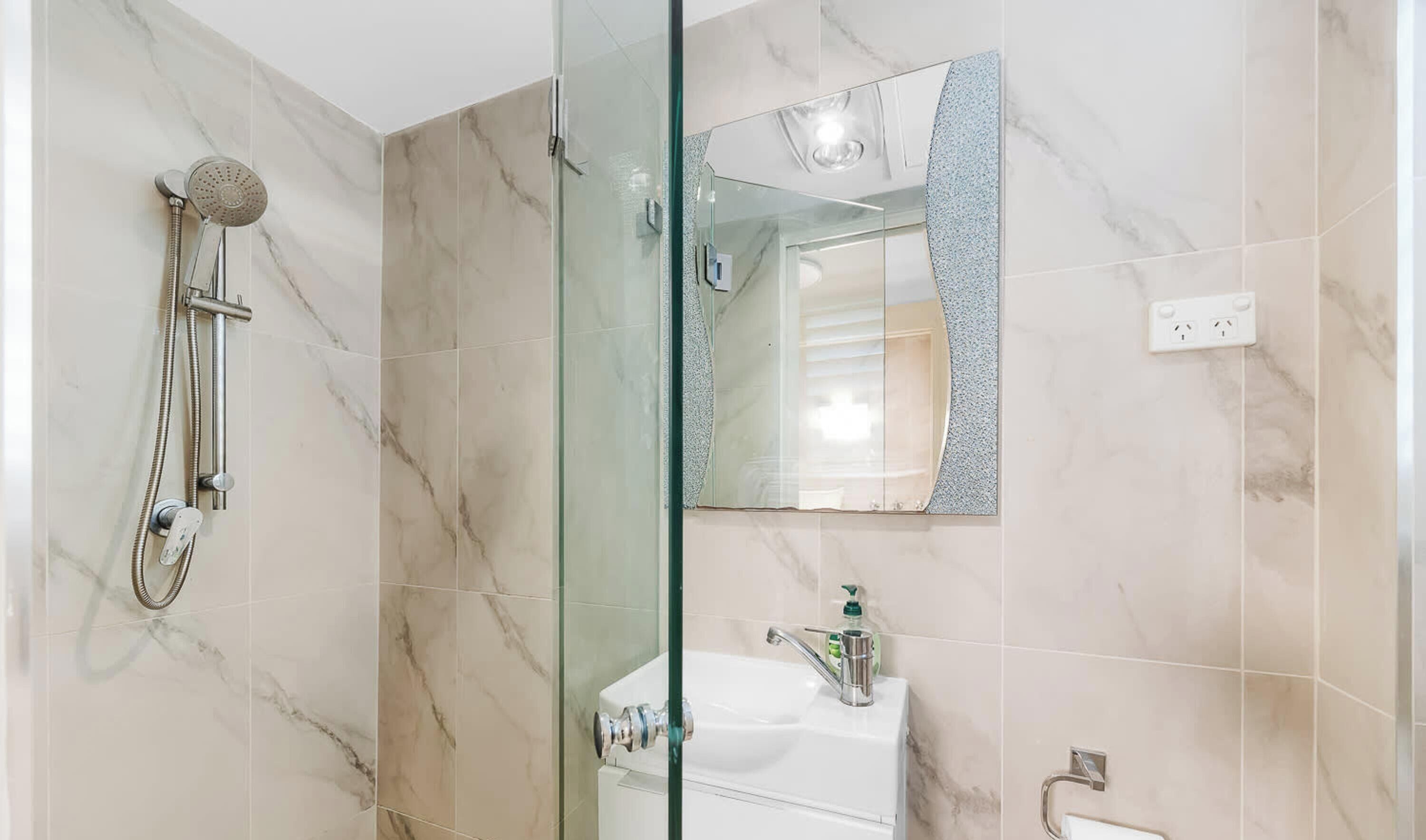A bathroom with a glass shower enclosure, a sink, and a mirror.