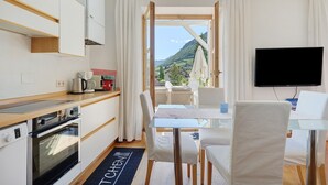 A modern kitchen with built-in appliances, a dining area with a glass table, and a TV mounted on the wall. - Apartment 'Sonnenresidence Alpenhof' with Mountain View, Balcony and Wi-Fi (Termeno sulla Strada del Vino)