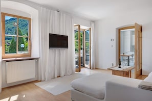 A bedroom with a large window, a flat-screen TV, a bed, a small table with a bottle and glasses, and a mirror. - Apartment 'Sonnenresidence Alpenhof' with Mountain View, Balcony and Wi-Fi (Termeno sulla Strada del Vino)