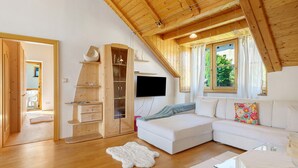 Ein modernes Wohnzimmer mit Holzboden, einem weißen Sofa, einem Glastisch und einem an der Wand befestigten Fernseher.