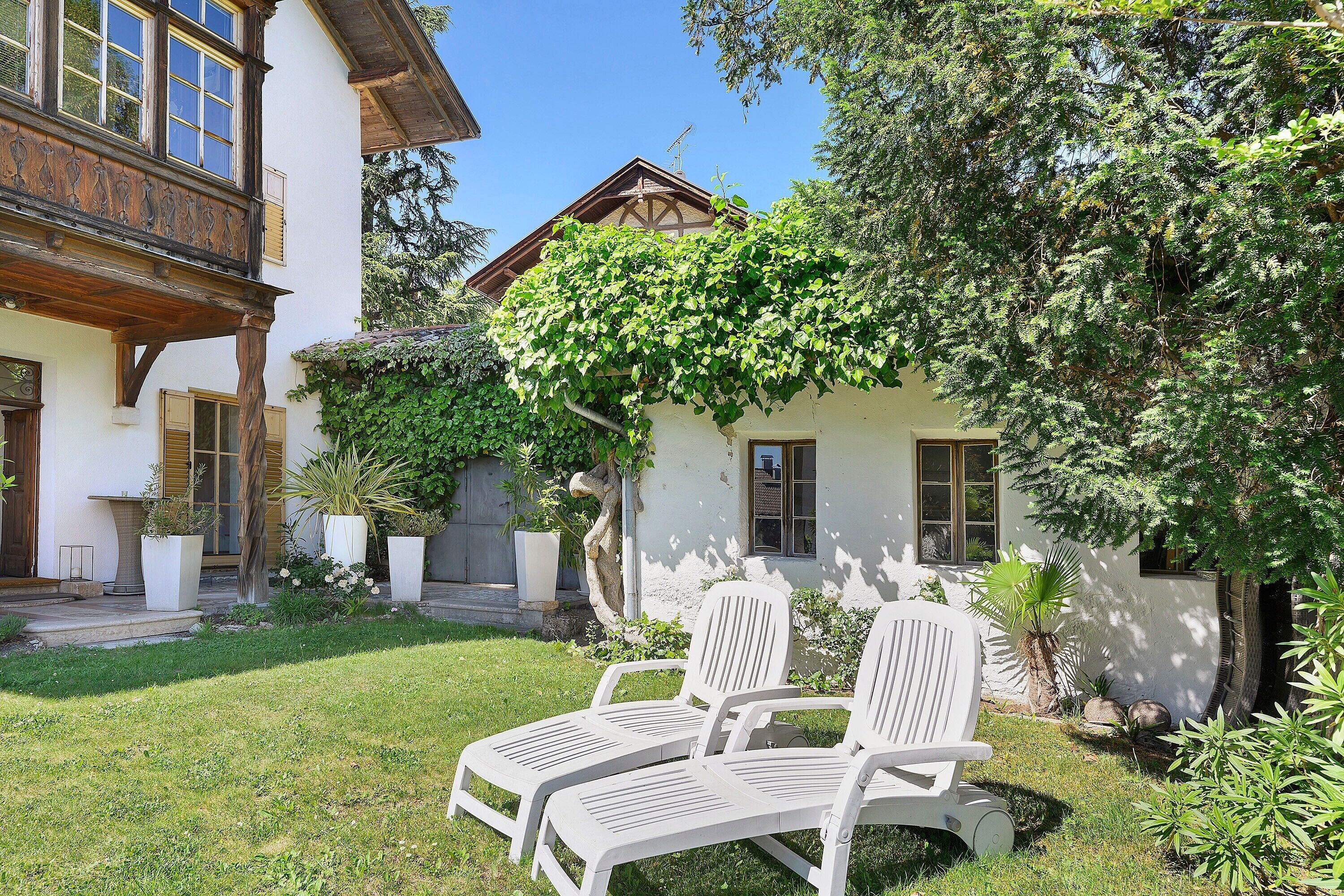 Ein Innenhof mit einem weißen Stuhl, einem Gebäude mit Balkon und einem Baum mit grünen Blättern.