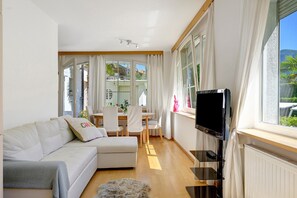 Un soggiorno moderno con divano, televisore, zona pranzo e ampie finestre.