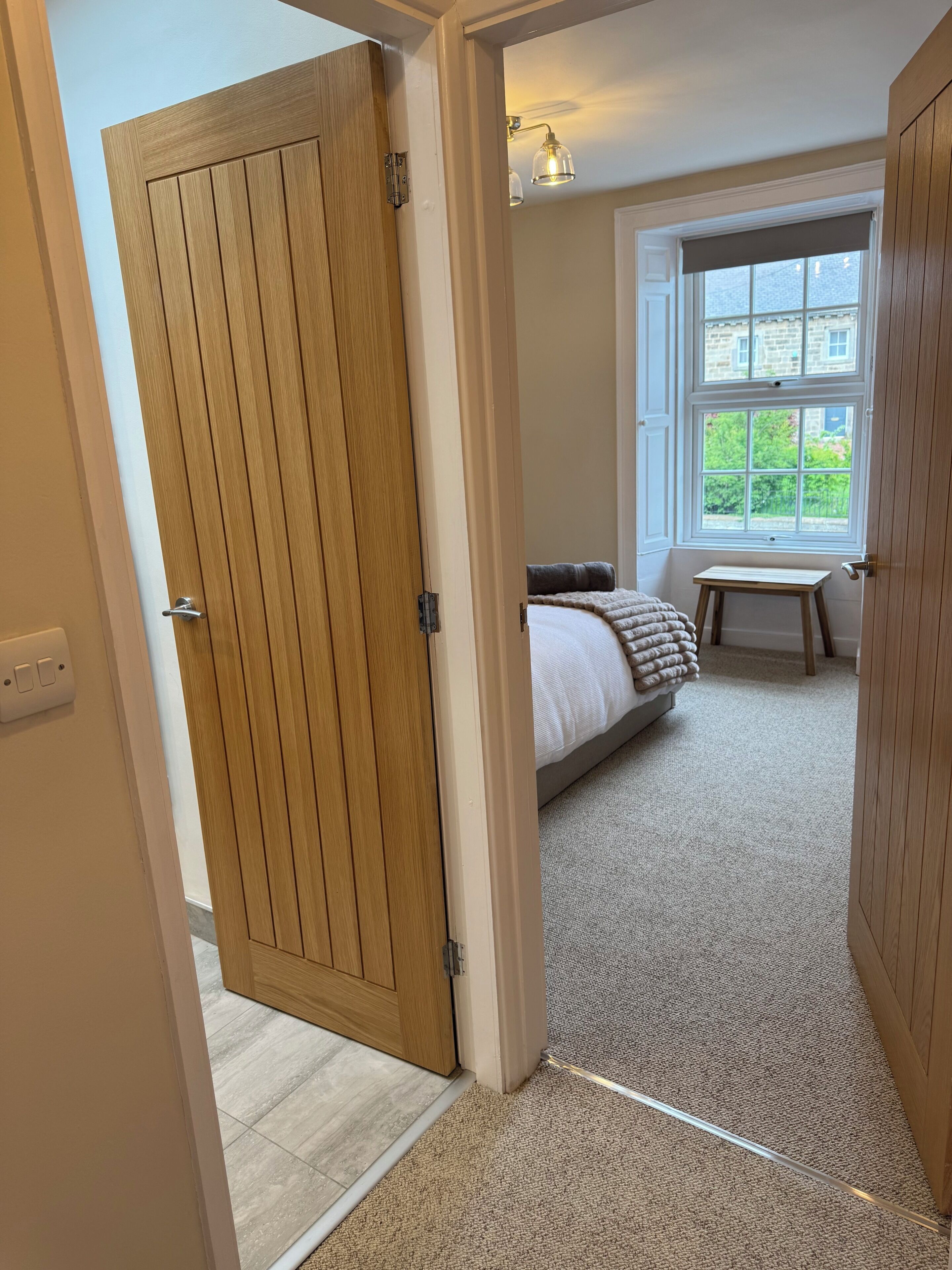 A bedroom with a bed, a small table, a window with a view, and a wooden door.