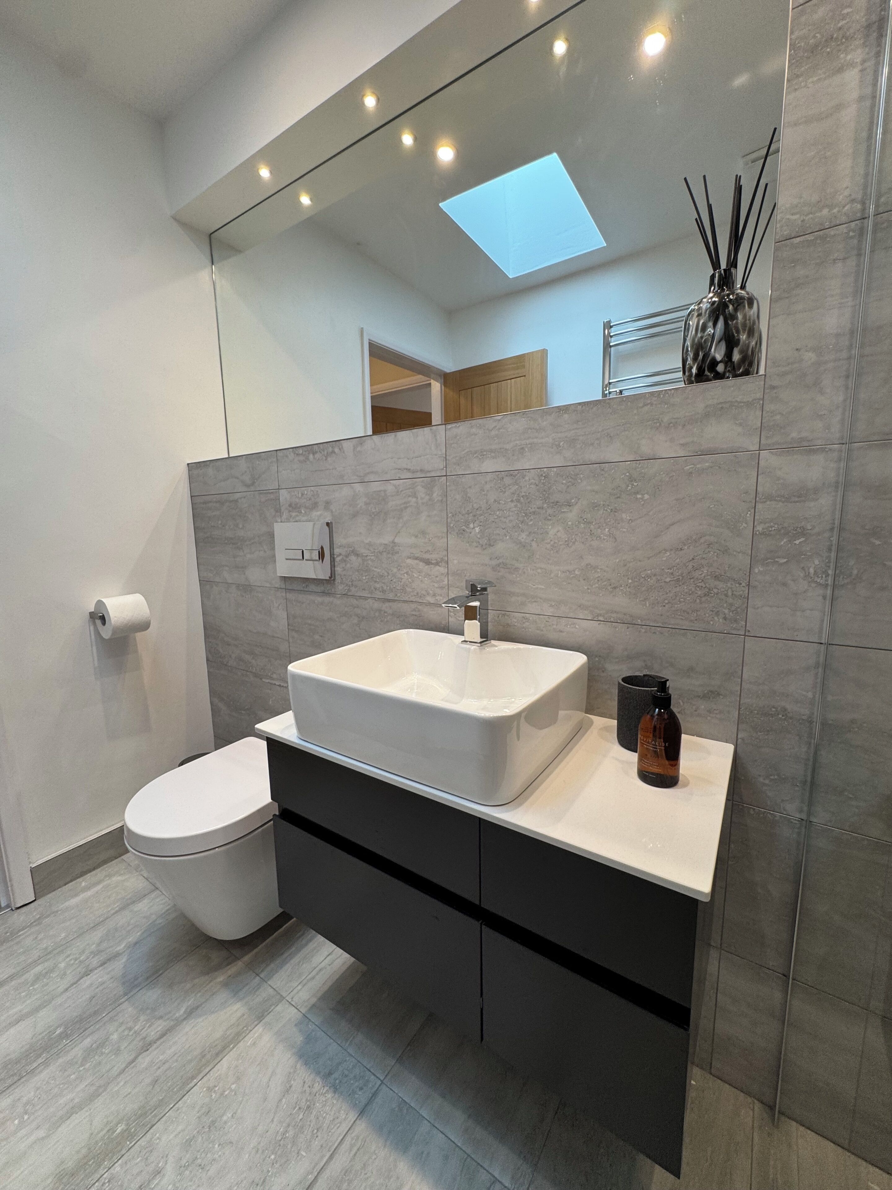 Een moderne badkamer met een wit wastafelmeubel, toilet, spiegel en dakraam.