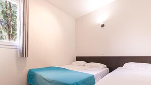 A small, clean room with two single beds, a window with curtains, and a wall-mounted light. - Family Villa Near Favone Beach (Sari-Solenzara)