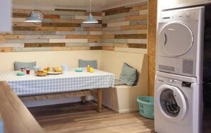 A compact kitchen with a washing machine, a dining table with a checkered tablecloth, and a wooden wall panel.