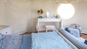 A tented room with a bed, a desk, a chair, a small table, a fan, and a window. - Yurt with Private hot tub and bathroom (Marshwood Dorset)