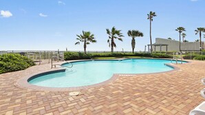 A swimming pool with a brick deck, palm trees, and a fence. - 9th Floor Beachfront Condo w/ Pool, Hot Tub, Sauna, & Beach Access! (South Padre Island)
