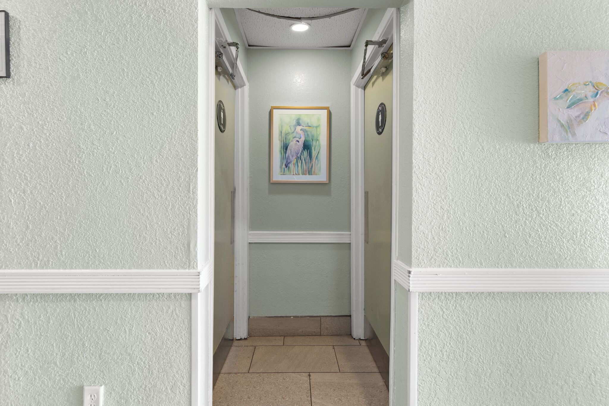 A hallway with a framed painting on the wall, white trim, and a light switch on the left.
