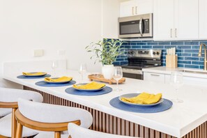 Eine moderne Küche mit weißen Schränken, einer blauen Spritzschutzwand und einer zentralen Kochinsel mit blauen Tischsets und gelben Servietten.