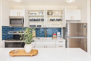 Eine moderne Küche mit weißen Schränken, einem Edelstahl-Kühlschrank, einer Mikrowelle und einer blauen Küchenzeile.