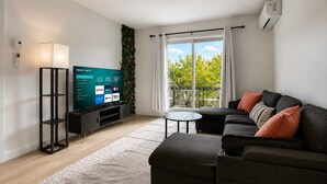 A modern living room with a flat-screen TV, a sofa, a coffee table, and a balcony with a view. - Boho Chic, 3 Bedrooms + Parking + AC | U8 (Québec City)