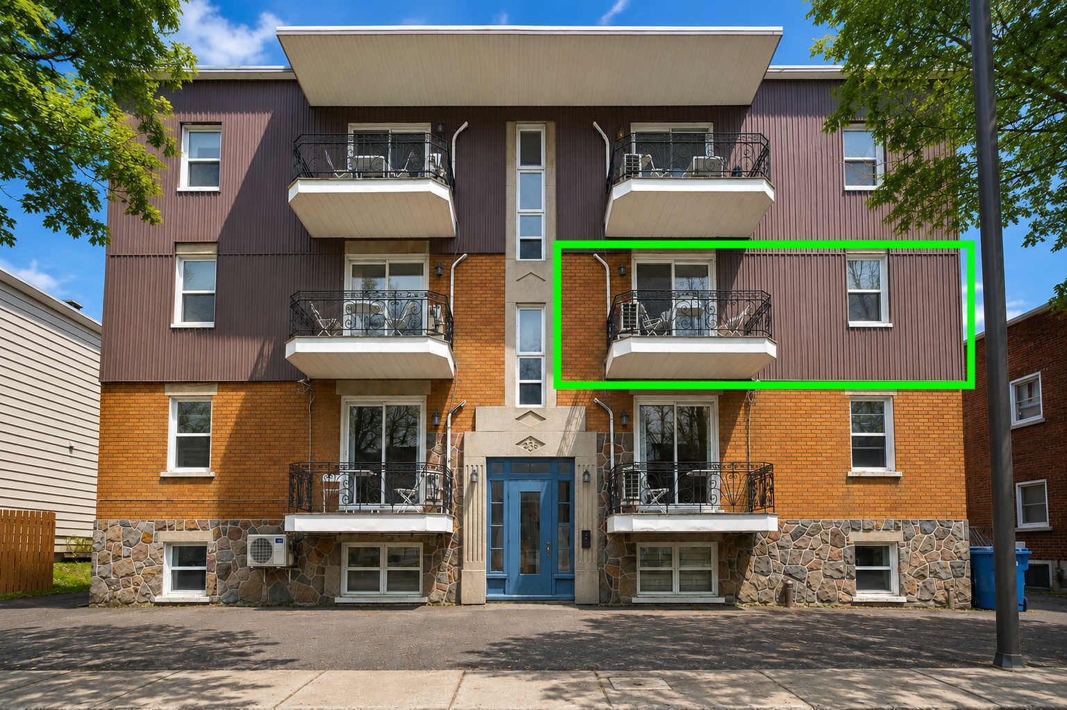 Un edificio de apartamentos de varios pisos con entrada central, base de piedra y balcones en cada planta.