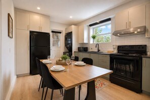 A modern kitchen with a dining table, chairs, a refrigerator, microwave, stove, and cabinets. - 3BR Close to centre + Parking + AC | Unit 6 (Québec City)