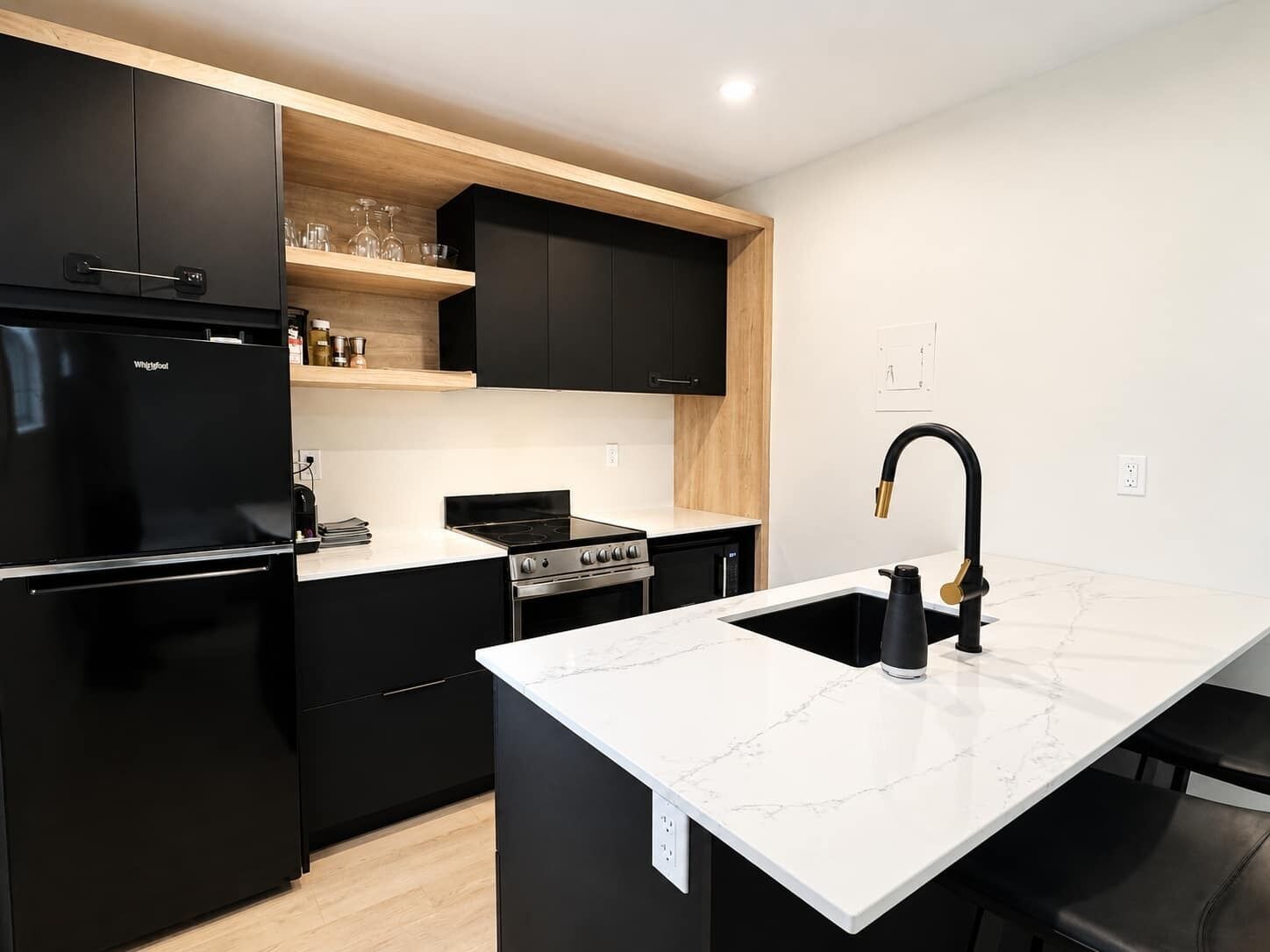 A modern kitchen with black appliances, a white marble countertop, and a black faucet.