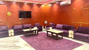 Ein Zimmer mit einem großen Flachbildfernseher an der Wand, einer Sofagarnitur, einem Couchtisch und einem gemusterten Teppich.