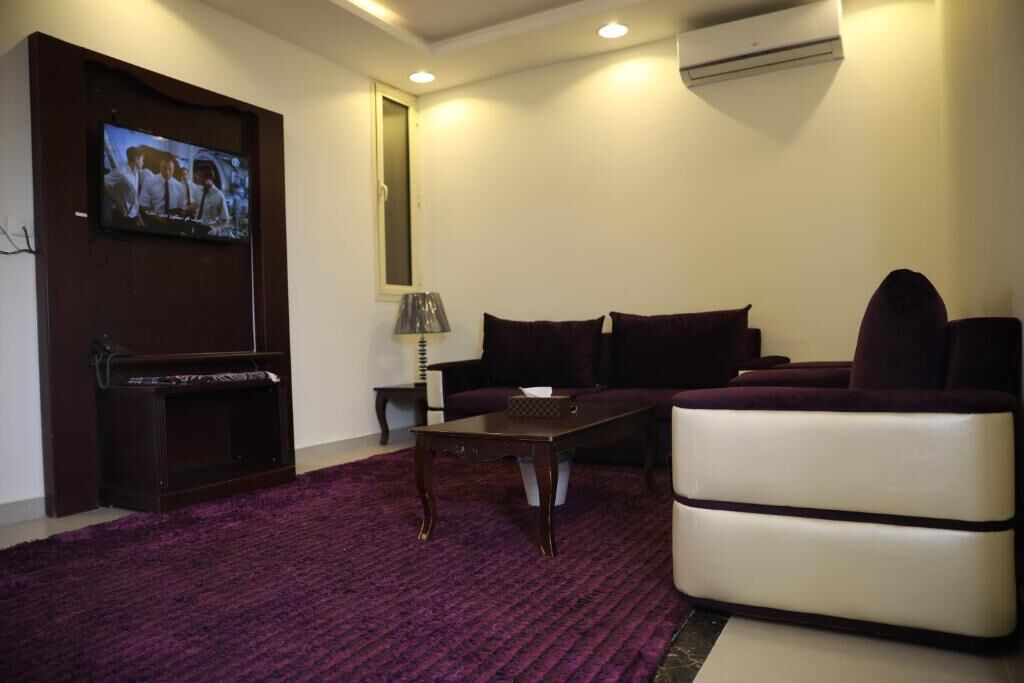 A living room with a flat-screen TV, a dark-colored sofa, a coffee table, and a purple carpet.