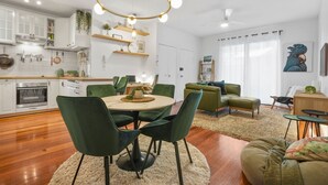 Una cucina moderna con mobili bianchi, una zona pranzo con sedie verdi e un soggiorno con divano verde.