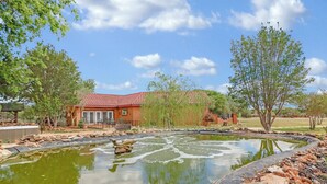 A house with a red roof, a pond with a fountain, and surrounding trees. - Private Hot Tub, Firepit & Duck Pond Near Canyon Lake + Whitewater Amphitheater (Canyon Lake)
