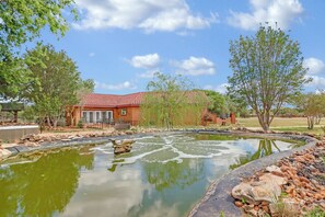 A house with a red roof, a pond with a fountain, and surrounding trees. - Private Hot Tub, Firepit & Duck Pond Near Canyon Lake + Whitewater Amphitheater (Canyon Lake)