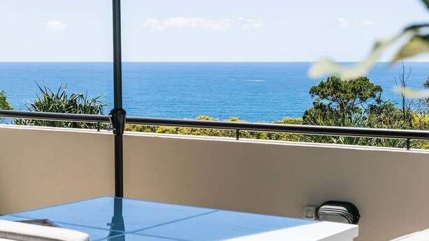 A balcony with a table and chairs, an umbrella, and a view of the ocean. - Ocean Outlook at Coolum (Coolum Beach)