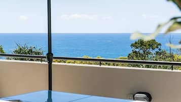 A balcony with a table and chairs, an umbrella, and a view of the ocean.