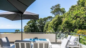 A terrace with outdoor furniture, a table, and a large umbrella. - Ocean Outlook at Coolum (Coolum Beach)