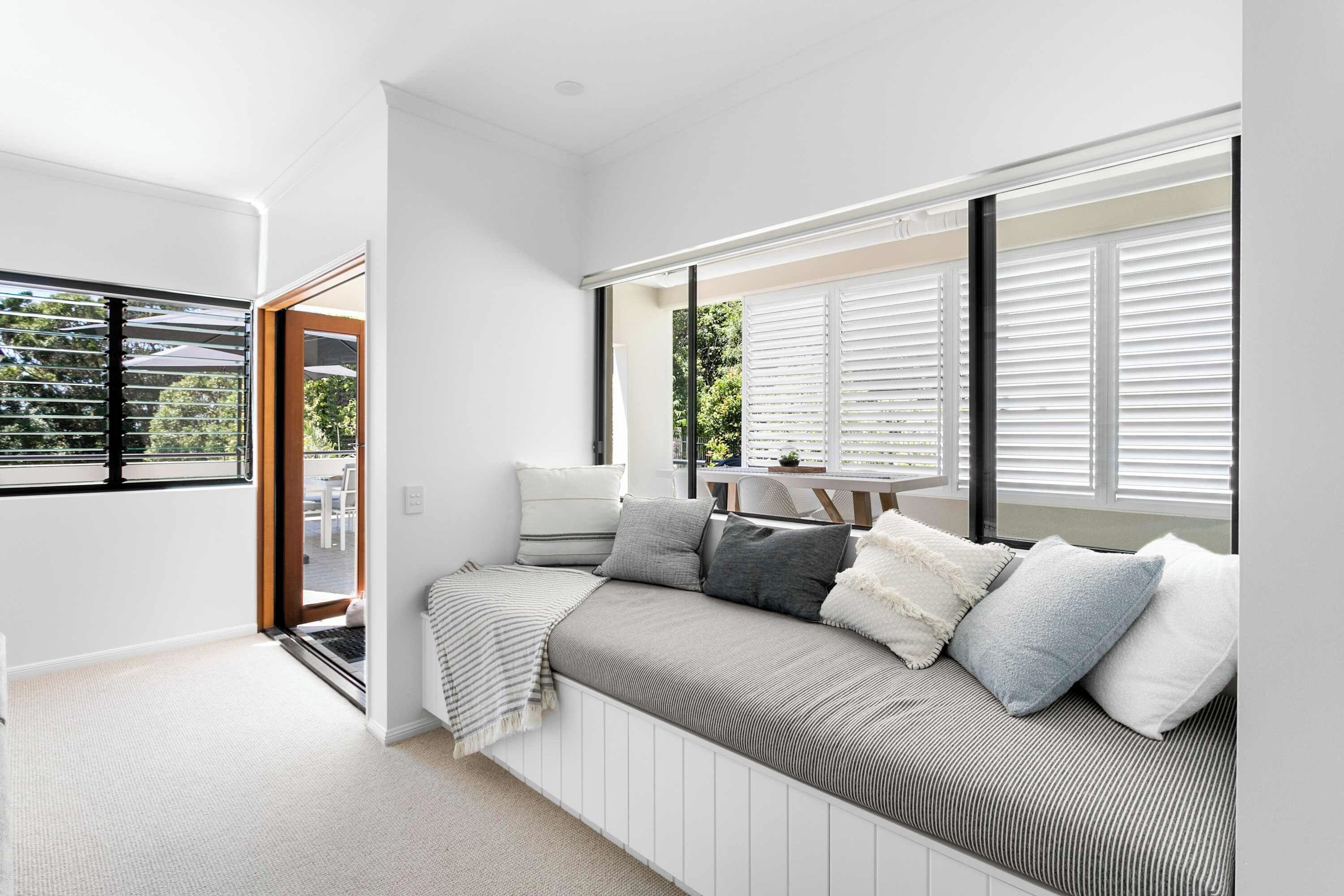 A modern room with a built-in bench, large windows with blinds, a door leading outside, and a view of greenery.