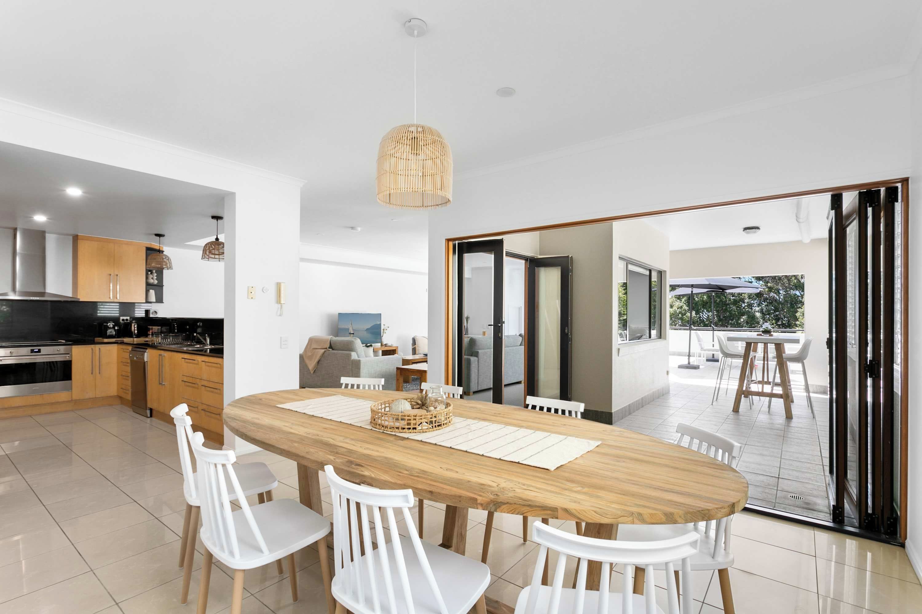 A modern kitchen with a dining area, a large wooden table, and white chairs.