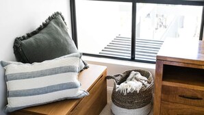 A room with a wooden bench, a striped pillow, a woven basket with a white blanket, and a view of a staircase through a window. - Ocean Outlook at Coolum (Coolum Beach)