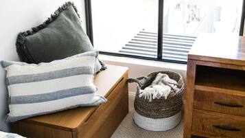 A room with a wooden bench, a striped pillow, a woven basket with a white blanket, and a view of a staircase through a window.