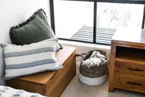 A room with a wooden bench, a striped pillow, a woven basket with a white blanket, and a view of a staircase through a window. - Ocean Outlook at Coolum (Coolum Beach)
