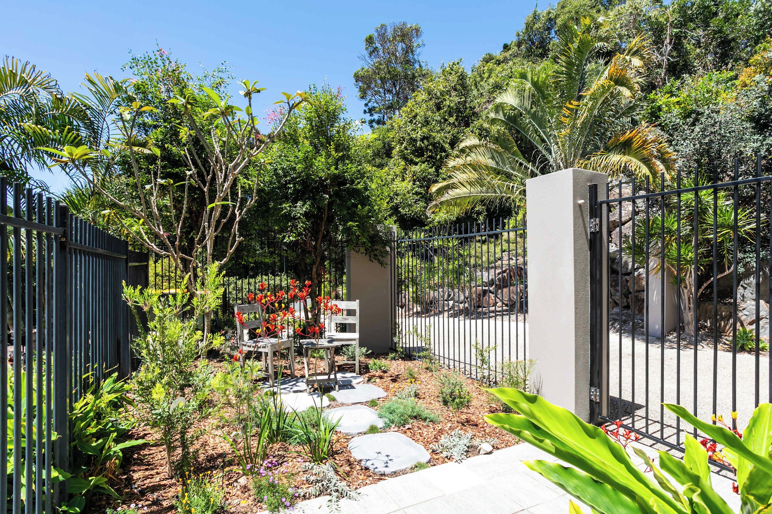A garden with a paved walkway, a metal fence, and a bench.