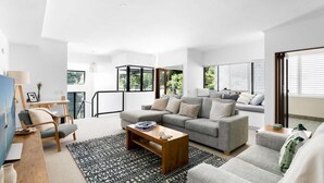 A modern living room with a sofa, coffee table, and a view of greenery outside. - Ocean Outlook at Coolum (Coolum Beach)