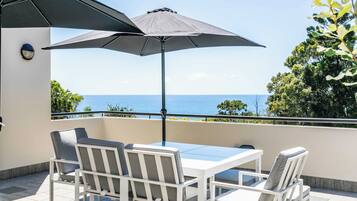 A balcony with a table and chairs, a large umbrella, and a view of the sea.