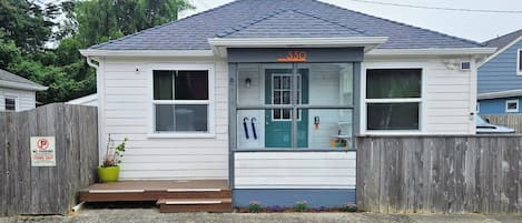 A charming coastal cottage with a welcoming teal door, wooden deck, and peaceful residential setting provides the perfect home base for your getaway.