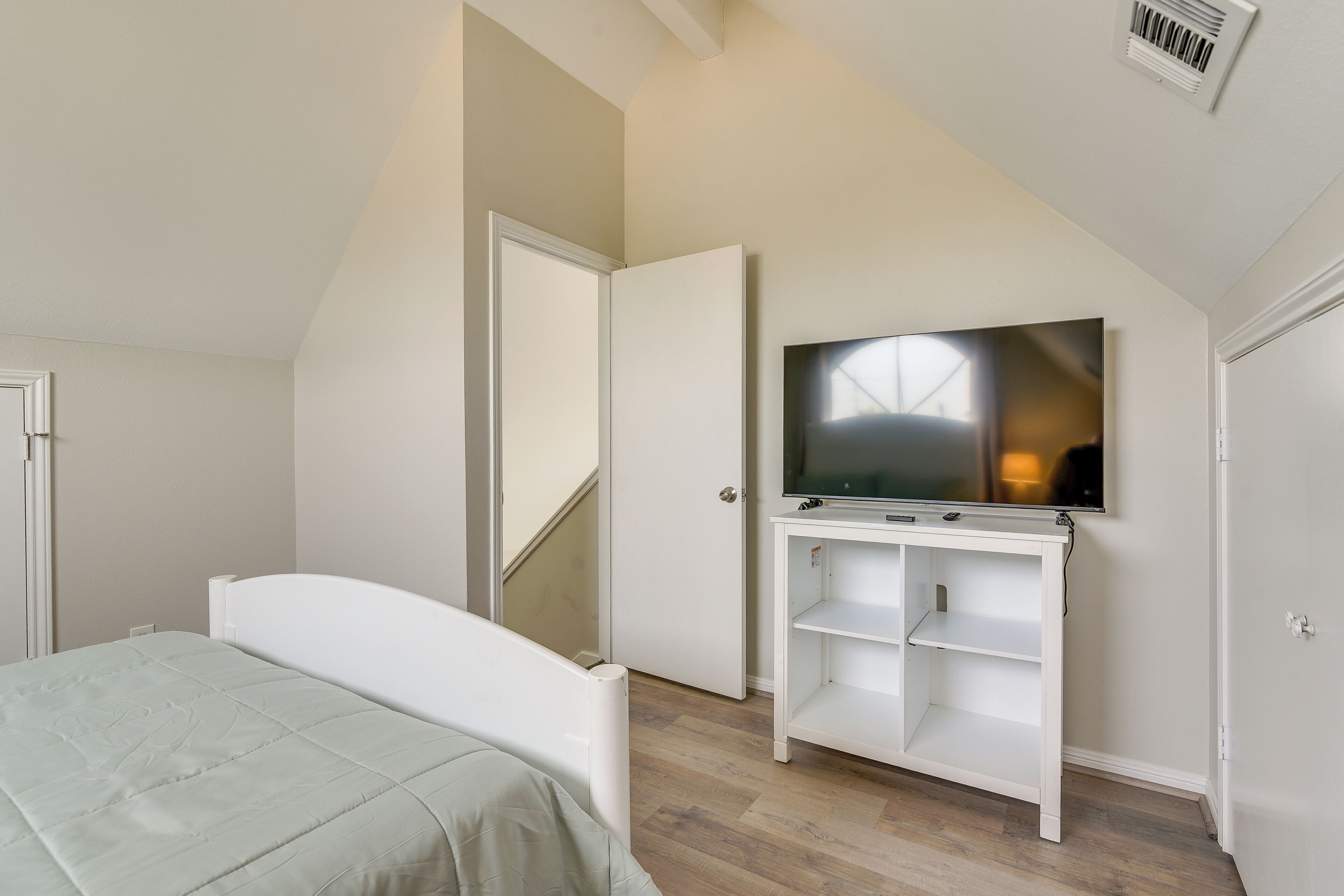 Een slaapkamer met een bed, een televisie op een witte standaard, een deur en een schuin dak.
