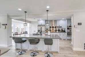 Cozinha moderna com ilha central, banquetas, eletrodomésticos de aço inoxidável e iluminação pendente.