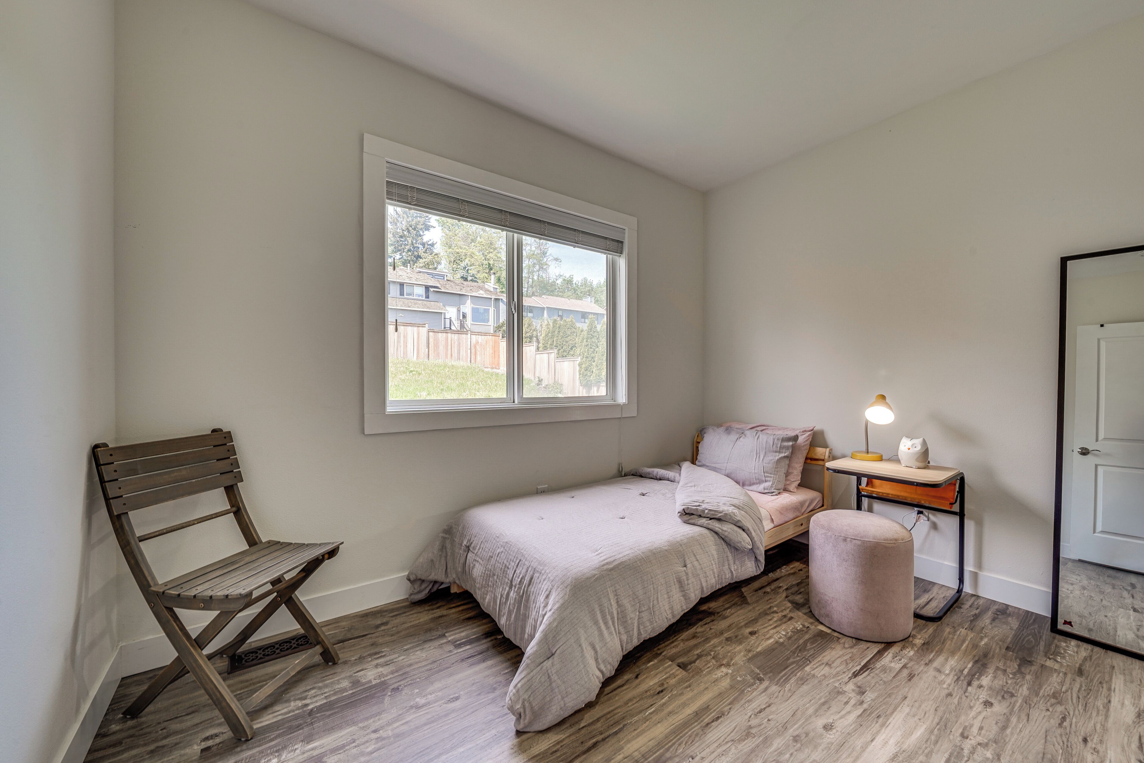 A bedroom with a single bed, a nightstand, a chair, a window, and a door.