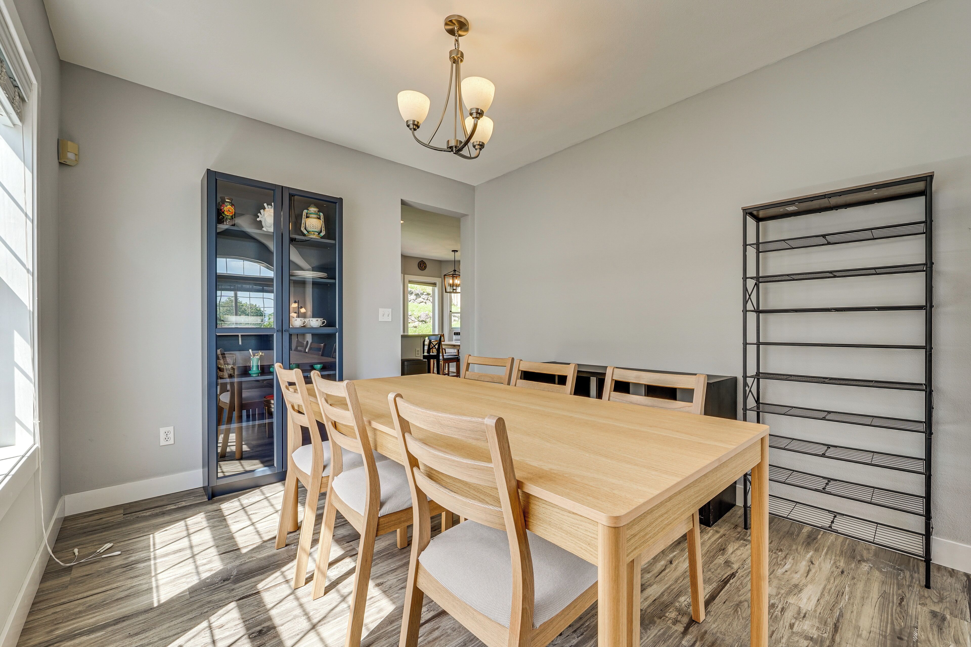 Un espace repas comprenant une table et des chaises en bois, un lustre et un présentoir en métal.